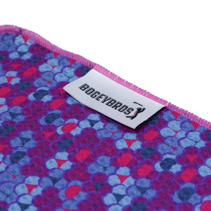 A close-up of the Whale Tail - Towel shows colorful overlapping purple, blue, and pink dots, pink-edged stitching, a white BOGEYBROS tag with golfer silhouette, plus a clip and eyelet for easy attachment.