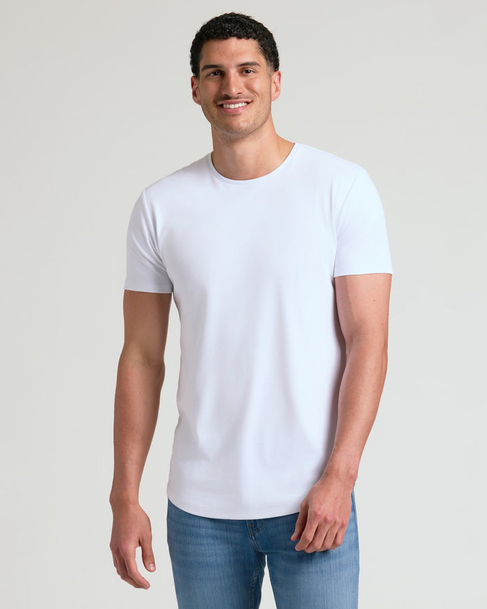 A smiling man wearing a white Tall Pima Cotton Blend Curved Hem Crew 4-Pack shirt paired with blue jeans, showcasing a clean and comfortable men's basics style.