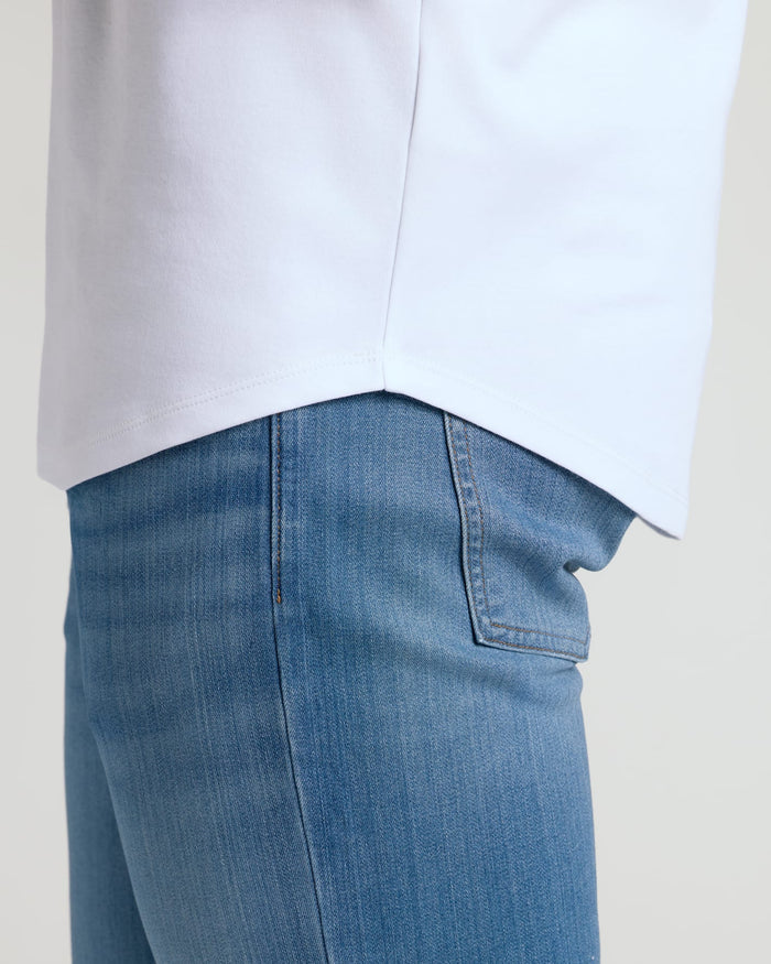 Close-up of the curved hem on a white Tall Pima Cotton Blend Curved Hem Crew 7-Pack shirt worn with blue denim jeans, showcasing the shirt's clean, tailored edge.